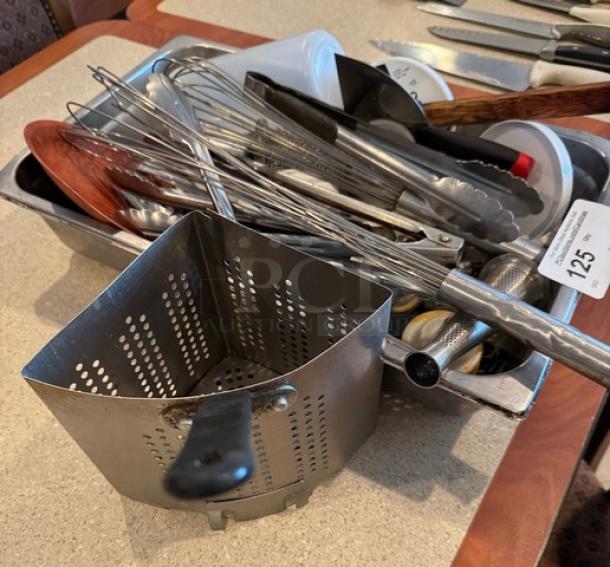 Assorted kitchen utensils including whisks, tongs, and a pasta strainer, in good condition. Auction tag numbered 125.