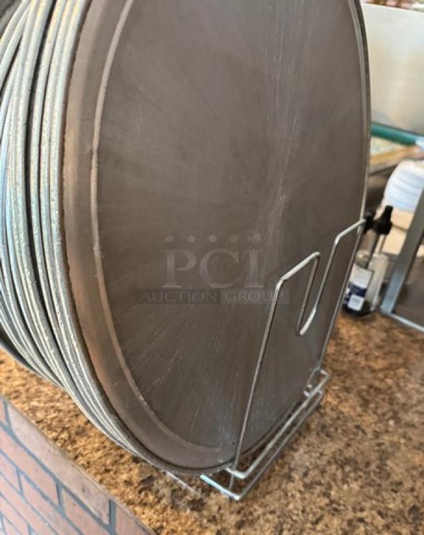 Assorted round pizza pans in metal rack, used condition, with visible wear. Essential for pizzerias or baking enthusiasts.