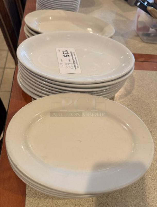 Assorted oval ceramic platters and plates in various sizes, stacked. Auction lot tag indicates "Lot #135." Good condition.