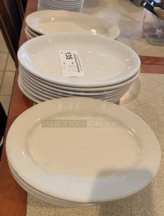 Assorted oval ceramic platters and plates in various sizes, stacked. Auction lot tag indicates "Lot #135." Good condition.