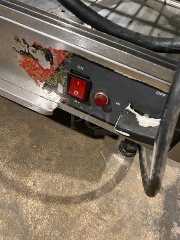 Commercial stainless steel electric countertop heated merchandiser display case with wired racks and legs. Visible wear on exterior.