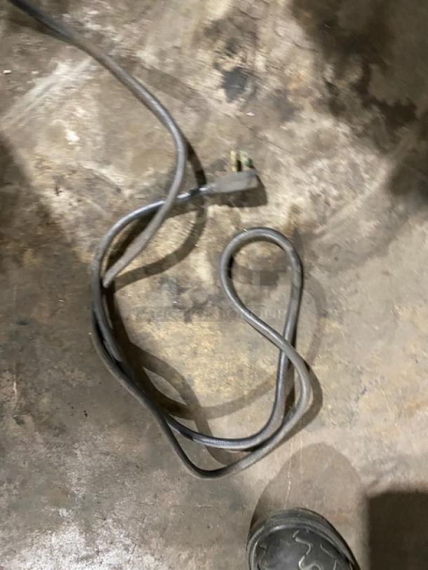 A power cord lies loosely coiled on a concrete floor, next to a shod foot.