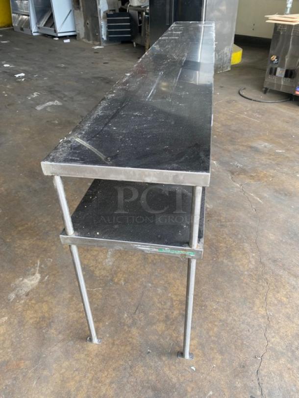 Stainless steel commercial double overhead work shelf, 10 feet long, heavy-duty construction, shows wear, ideal for kitchen use.