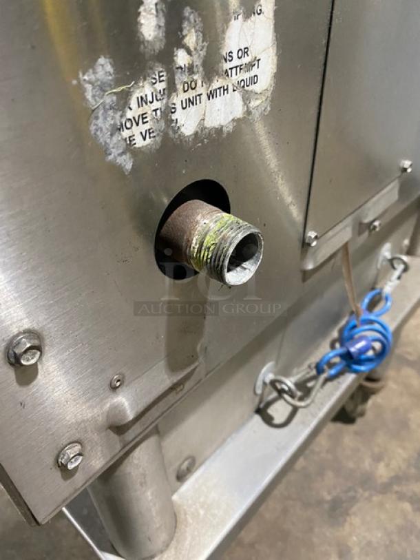Keating stainless steel natural gas griddle back view, showing a connection point and worn label. Griddle is on caster cart.