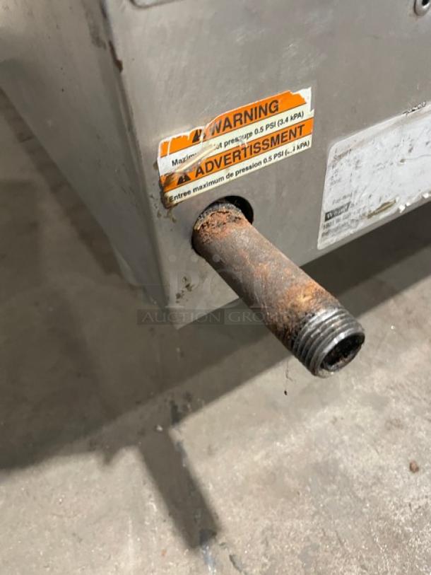 Woodstone stainless steel natural gas countertop grill with rusty gas inlet, warning label for pressure limits visible.