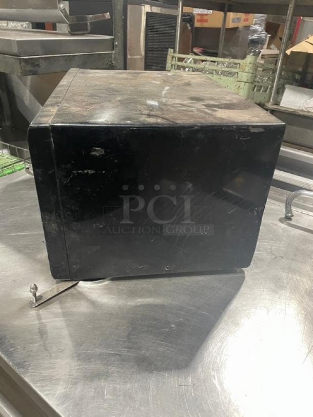 Oster OGZJ1104 black countertop microwave oven, commercial grade, digital controls, 120V, visible wear on exterior.