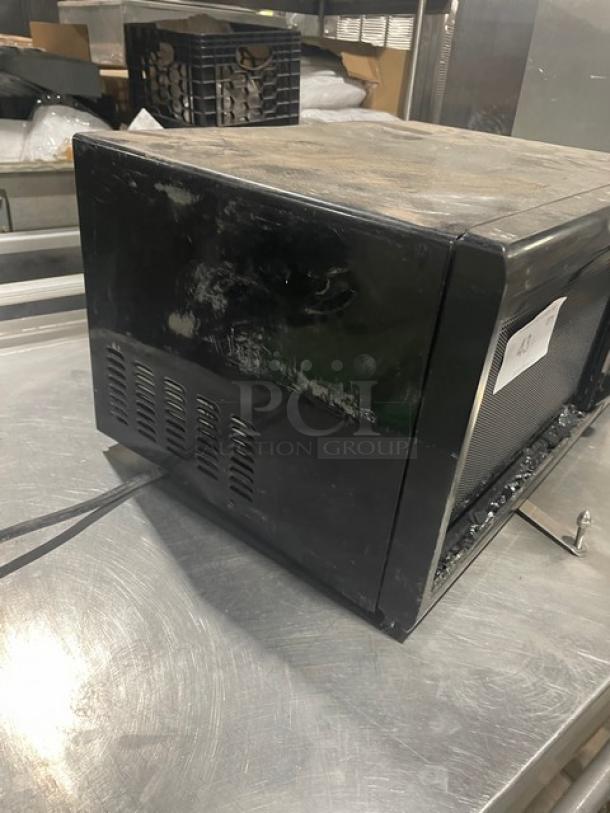 Oster OGZJ1104 black countertop microwave oven with digital controls. Visible wear on surface. Model number on label.