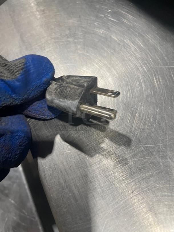 Close-up of a black two-prong plug held by a gloved hand, associated with the Oster OGZJ1104 microwave oven.