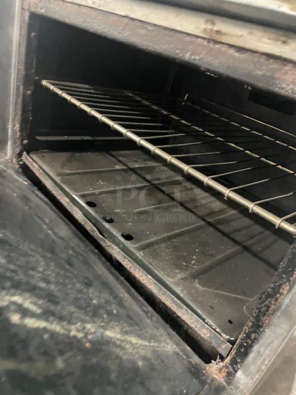 Commercial stainless steel gas-powered char broiler range/oven combo with a wired oven rack, showing signs of wear.