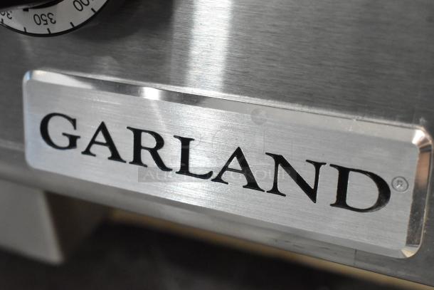 "Garland stainless steel flat top griddle, brand new, minor scratches and dents, natural gas powered, label visible."