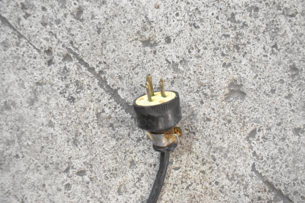 Power plug for the True TWT-72 commercial cooler, featuring a black, three-pronged plug on a textured concrete surface.