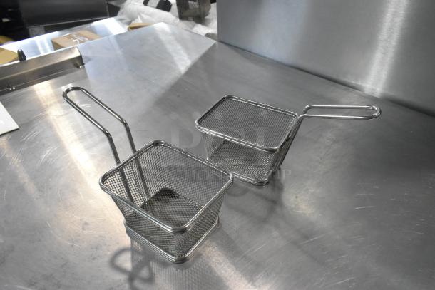 Two metal mini baskets with handles, made of wire mesh, displayed on a stainless steel surface.