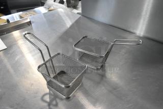 Two metal mini baskets with handles, made of wire mesh, displayed on a stainless steel surface.