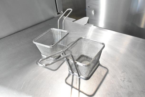 Two metal mini baskets with handles on a stainless steel surface, showcasing mesh design and ideal for serving or small storage.