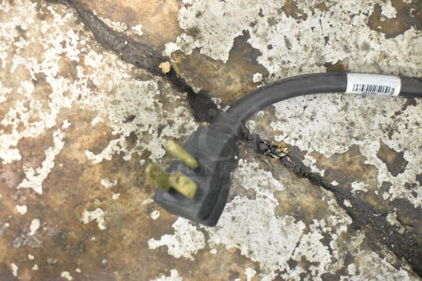 Power cord of True T-19F freezer with a three-prong plug on a worn, textured surface.