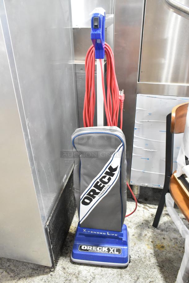 Brand new Oreck XL2100RHS upright vacuum, 12" wide, lightweight, bagged, with visible scratches and dents. 120V, 1 phase.