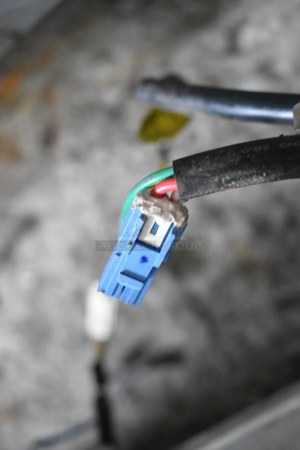 A close-up of a blue electrical connector with red and green wires attached, over a blurred background.