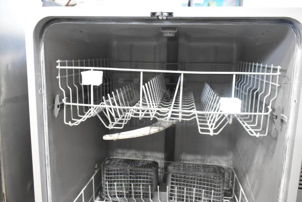 Stainless steel undercounter dishwasher, interior view, showing racks and compartments in clean condition.