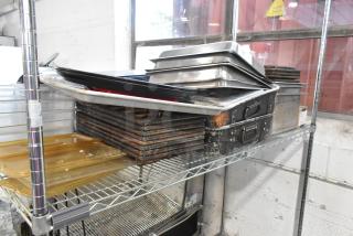 Auction lot of metal baking pans, stainless steel drop-in bins, and poly drop-in bin lids on a metal shelf. Signs of wear visible.