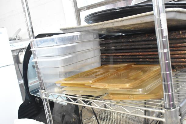 Metal baking pans, clear poly bins, and lids on stainless steel shelf. Items show moderate wear, ideal for kitchen use.