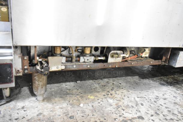Imperial commercial gas range underside showing gas connections and components. Stainless steel construction, some wear visible.