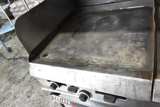Garland stainless steel commercial gas griddle with two sections, two ovens, overshelf, and backsplash, showing signs of use.