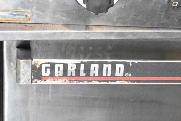 Garland stainless steel commercial gas griddle with two sections, two ovens, overshelf, and backsplash. Garland branding visible.