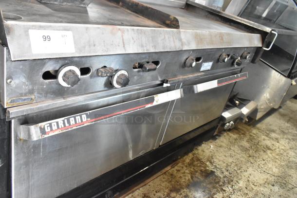 Garland stainless steel commercial gas griddle with two ovens, overshelf, and backsplash. Features include control knobs and visible branding. Moderate wear.