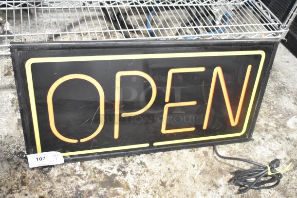 Illuminated "Open" sign, 115 volts, 1 phase. Rectangular, black background with neon lettering. Slight wear visible.