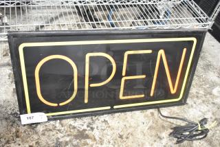 Illuminated "Open" sign, 115 volts, 1 phase. Rectangular, black background with neon lettering. Slight wear visible.