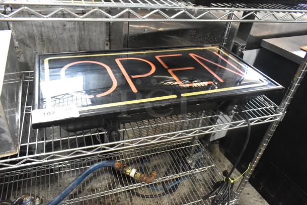 Illuminated open sign, 115 volts, 1 phase, neon lettering, mounted on metal shelf. Visible tag indicates item number 107.