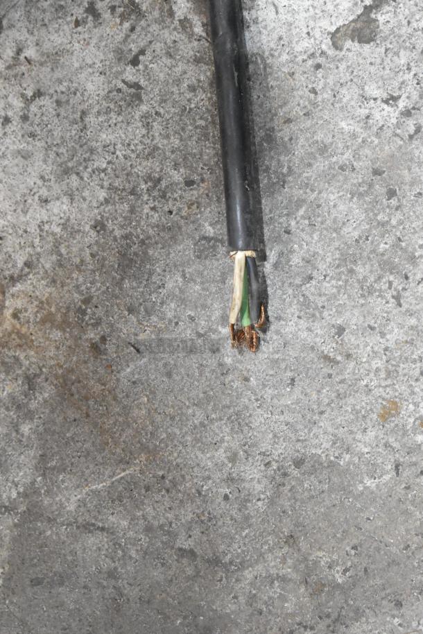 A damaged electrical cable with exposed wires on a concrete surface, requiring repair.