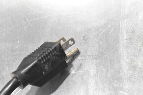 Alt Text: Close-up of a black electrical plug on a stainless steel surface.
