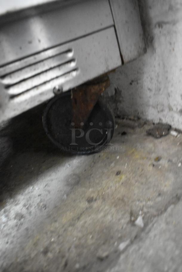 Close-up of a Beverage Air SP72-30M stainless steel prep table's caster on a concrete floor, showing slight rust.