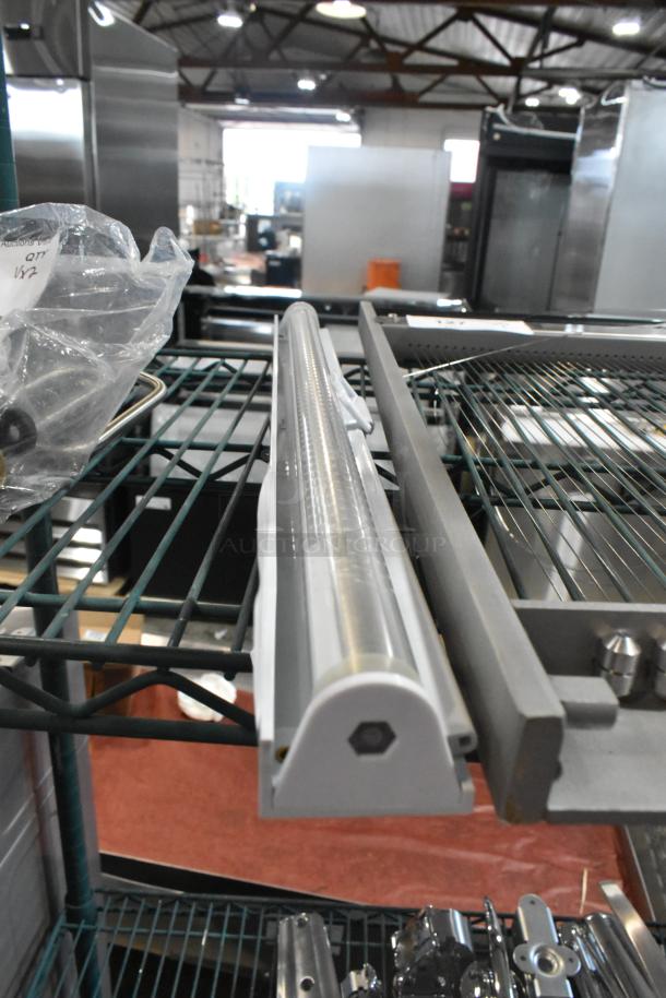 LED light strip with protective casing. Mounted on a metal rack in an industrial setting. Condition appears new.
