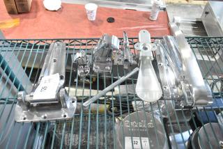 Four brand new scratch and dent items, including a hinge and door handle, displayed on a wire shelf, item tags visible.