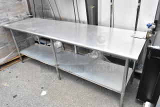 Stainless steel table with mounted commercial can opener and metal under shelf, in used condition, suitable for industrial kitchens.