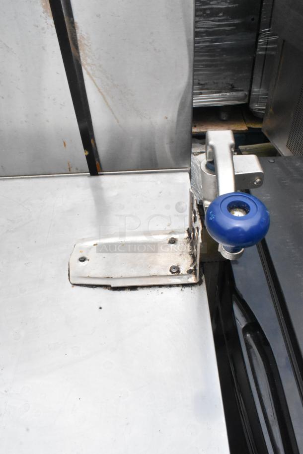 Stainless steel table with mounted commercial can opener and metal under shelf, showing signs of wear.