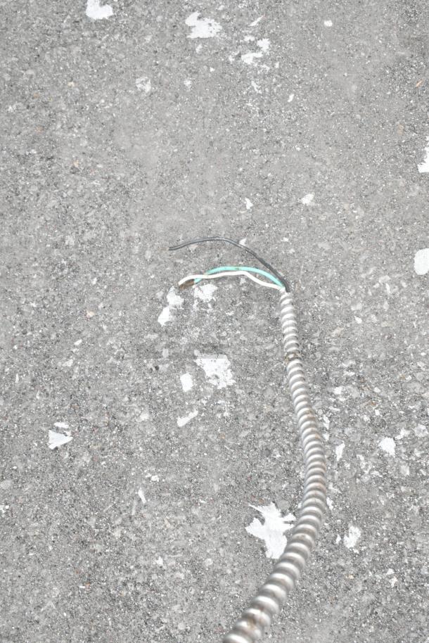 A close-up of a metal conduit on concrete ground, with exposed black, green, and white wires, possibly part of ventilation setup.