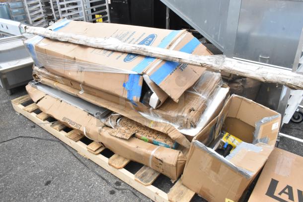 Boxes of Regency stainless steel scratch and dent items on a pallet, including pass-through shelves and commercial tables.