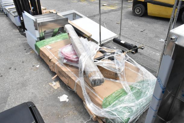 Four brand new scratch and dent items including Regency 64" black epoxy shelving post, Lancaster ruby red barstool, and Regency 30" x 84" stainless steel work table. All packaged together, visible wrapped in plastic.