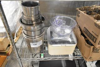 Brand new stainless steel cylindrical drop-in bins and food processor parts on a metal shelf. Auction tag marked "138."