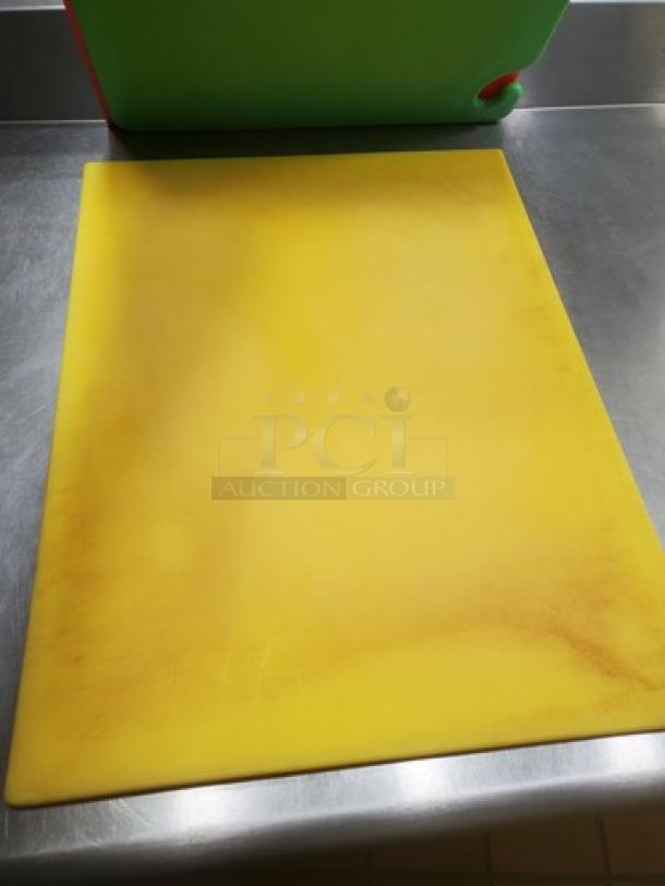 Lot of 3 cutting boards, featuring one large yellow board, lightly used, with visible surface marks, on a metal counter.