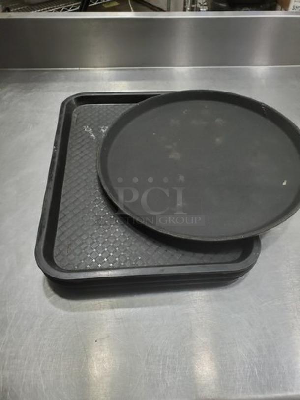 Lot of 5 black plastic serving trays, including round and rectangular shapes, showing minor wear.