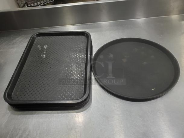 Lot of 5 black plastic serving trays including four rectangular with textured grip and one round. Used condition.