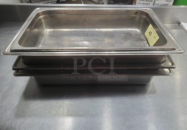 Lot of 5 stainless steel hotel pans, gently used, stacked on a metal surface. Auction tag visible.