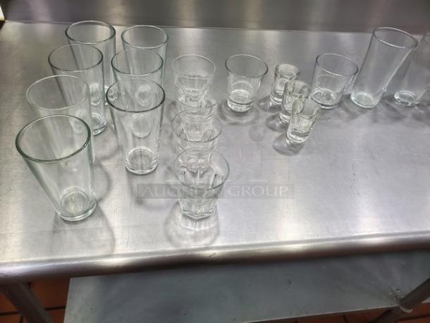 Lot of 26 miscellaneous glasses on a metal surface, featuring various sizes and styles, in good condition.