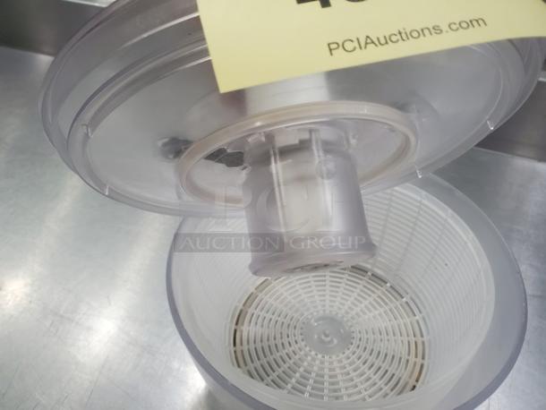 Clear plastic salad spinner with removable lid and basket, in good condition. Auction tag from PCI Auctions visible.