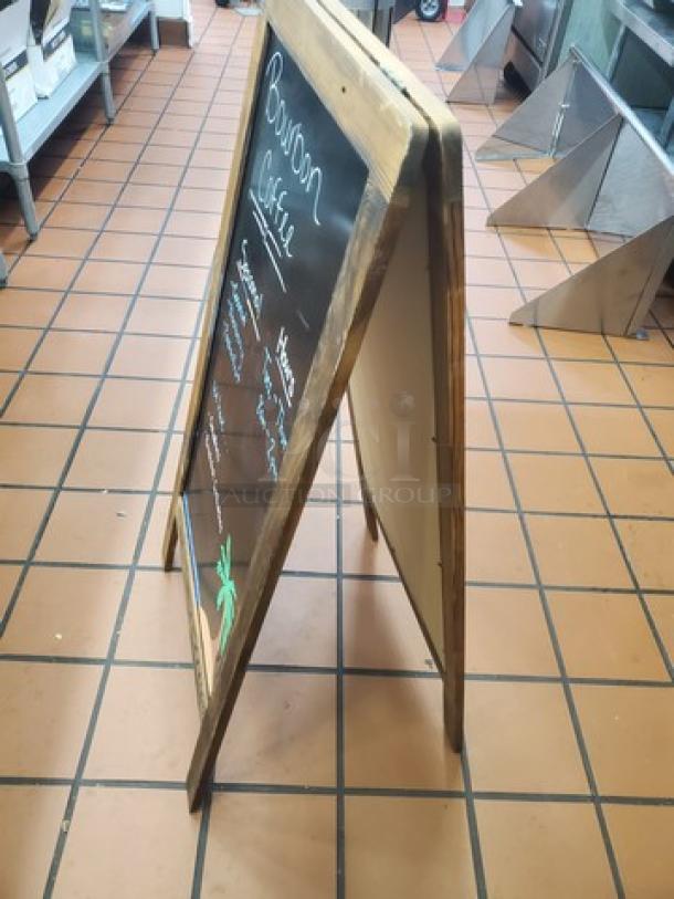 Wooden A-frame chalkboard sign with visible writing; used condition; sturdy frame with a blackboard surface for messages.