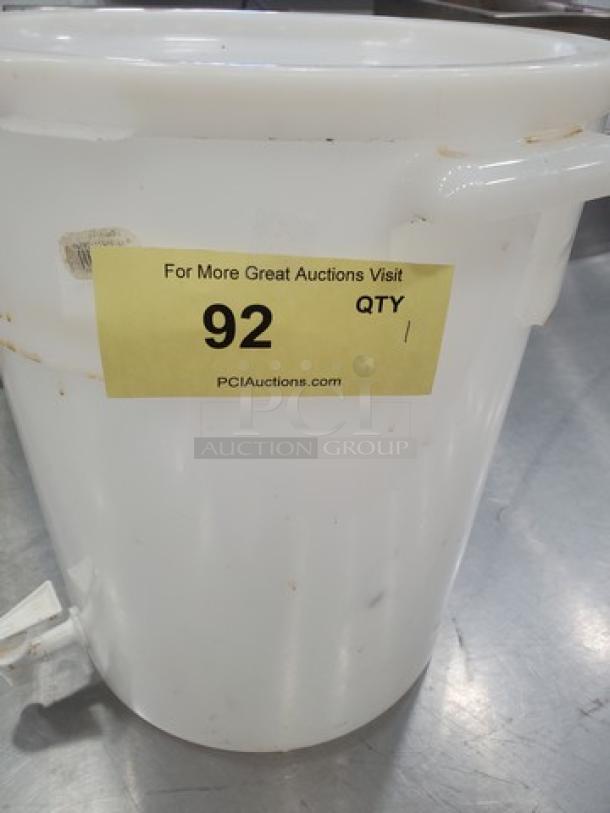 6-gallon white beverage dispenser with attached spigot, slight wear. Auction tag reads "92, PCI Auctions." Ideal for events.
